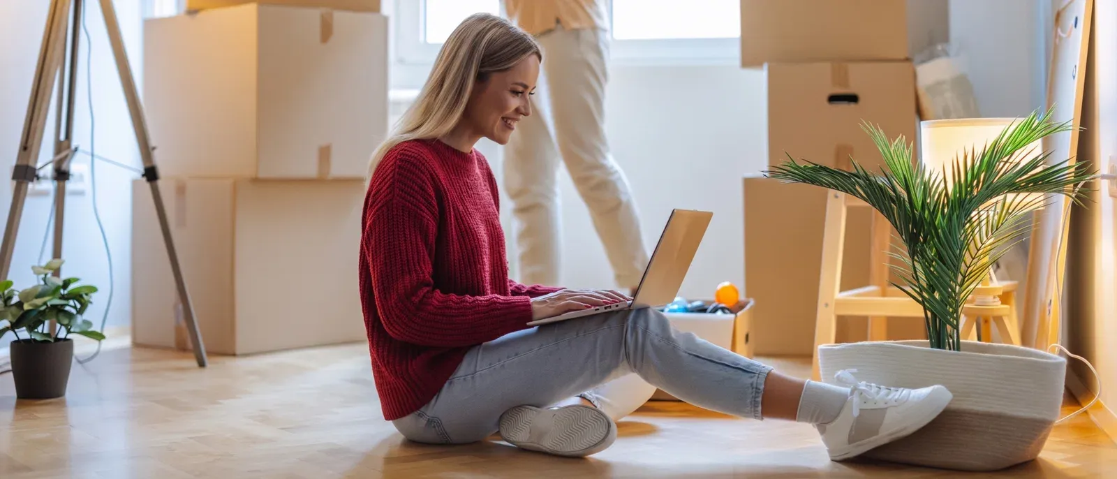 Woman sitting among moving boxes and using a laptop, signifying changing internet when she moves.